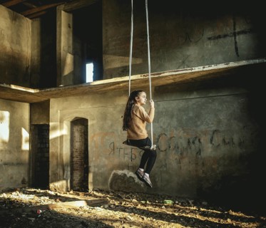 Girl rocking on a swing in a destroyed building on the seafront in Okhamchira