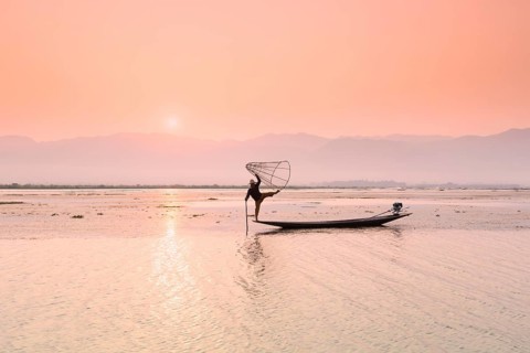 Inle lake fisherman standing on a longtail boat in the distinctive leg rowing stance used by the Intha people