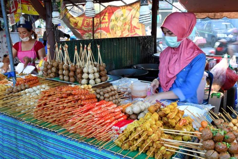 Saleswoman at the market stand with different skewers with meat and seafood