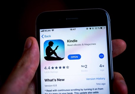 Hand holding an iPhone displaying the Amazon Kindle app