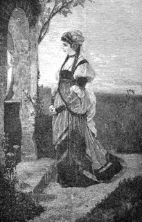 Woman stands in front of a small field chapel and prays