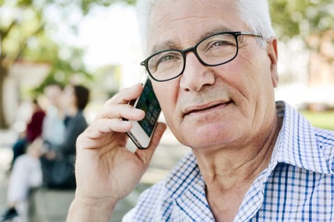 Grey-haired senior with glasses talking on the phone with his smartphone