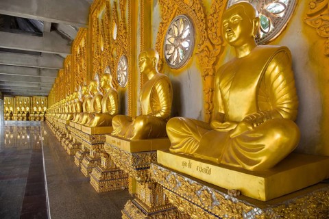 Row of golden Buddha statues in the corridor of the Phra Maha Chedi Chai Mongkhon Pagoda