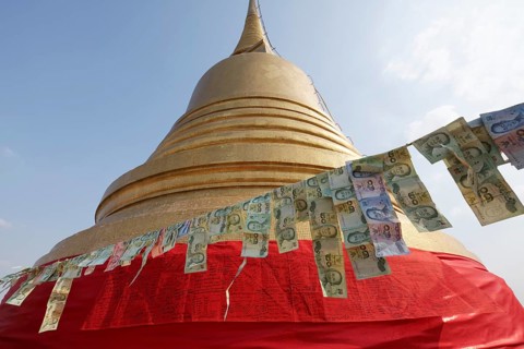 Thai banknotes are hanging on a leash in front of the golden Chedi