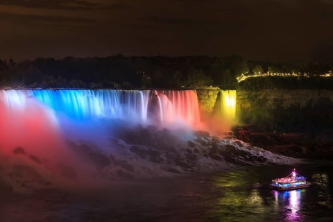 Tourist boat in front of illuminated waterfall