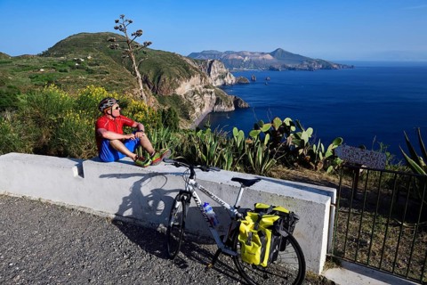 Cyclist pausing on the Belvedere Quattrocchi with a view over the rocks Faraglione on the island Vulcano
