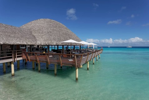 Restaurant on stilts with reed roof in turquoise sea