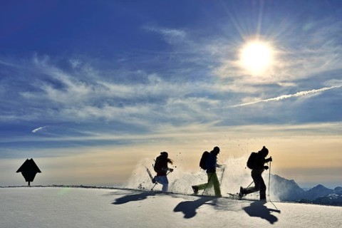 Three snowshoe walkers run in the snow against the light
