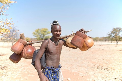 Young Himbamann carries water tank and food on the cattle drive