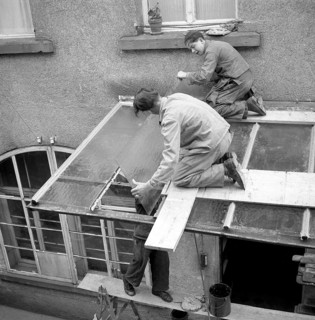Three roofers repair a canopy with glass panels