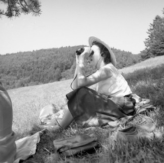 Woman sitting in nature looking through binoculars around 1950