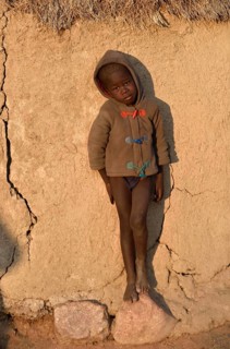 Himbajunge leans on mud hut