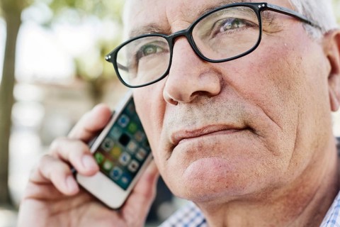 Grey-haired senior with glasses talking on the phone with his smartphone