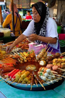 Saleswoman at the market stand with different skewers with meat and seafood