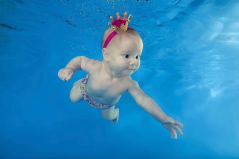 A little girl in a crown swims underwater in the pool