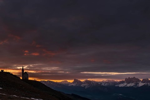 Latzfonser cross chapel at sunrise with dramatic clouds and South Tyrolean mountains