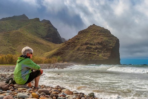 Tourist sits on the beach of Parque Ruben Perez in front of Charco de la Aldea