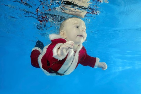 A little boy in Santa's cost swims underwater in the pool