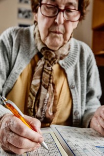 Senior sits at the table at home and solves puzzles