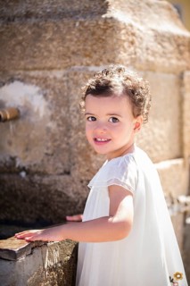Little girl in white dress stands by a fountain