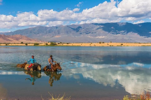 Nomad kids on horses crossing the Tuul river during summer time