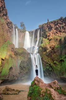 Young woman standing on a stone in front of Ouzoud waterfalls and cascades