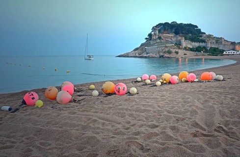 Orange and pink buoys on the sandy beach of Tossa de Mar