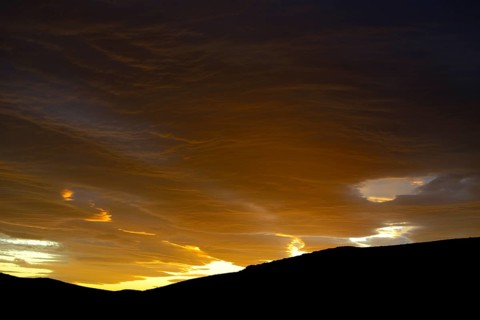 Dramatic sunset with rising storm clouds in front of mountain silhouette