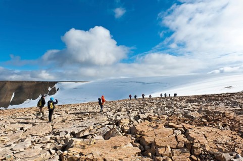 Hiking group in rocky terrain in front of Foxfonna glacier