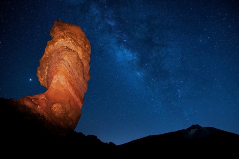Illuminated Roque Cinchado in front of Pico del Teide with starry sky
