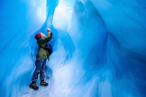 Woman photographing in a ice cave in Fox Glacier