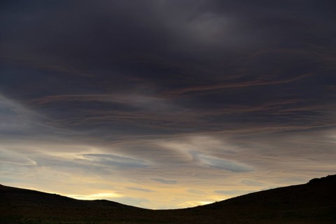 Dramatic sunset with rising storm clouds in front of mountain silhouette