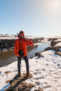 Man with camera equipment looking at Selfoss waterfall in winter