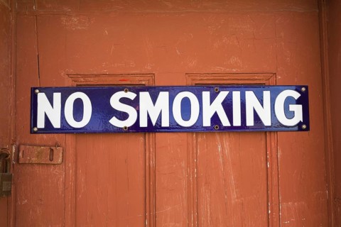 White and blue No Smoking sign on reddish brown wooden entrance door