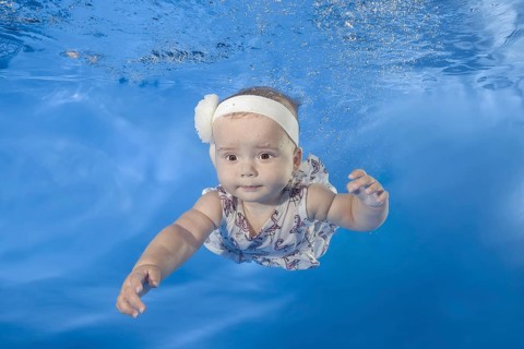 Little girl in a dress swims underwater in the pool
