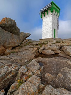 Green and white lighthouse on granite rocks