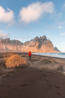 Man in red jacket walking on the black lava beach