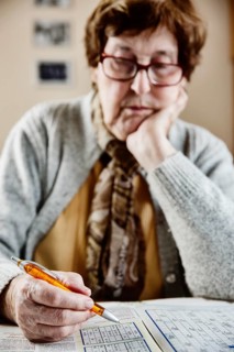 Senior sits at the table at home and solves puzzles