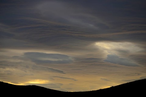 Dramatic sunset with rising storm clouds in front of mountain silhouette