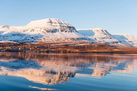 Water reflection of snow-covered mountains in a fjord