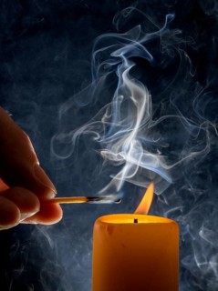 Lighting of a candle with smoking match in front of a black background