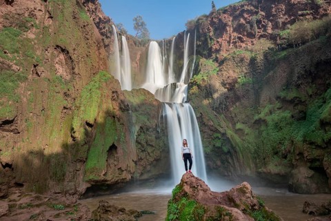 Young woman standing on a stone in front of Ouzoud waterfalls and cascades
