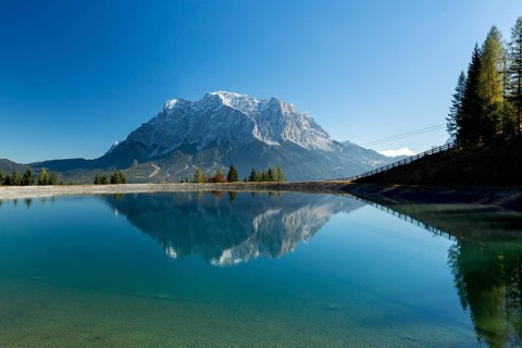 Water reservoir for snow production for the ski slopes on Grubigstein with view to the Zugspitze and mountain railway