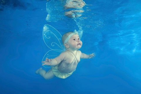A little girl in a fairy costume swims underwater in the pool