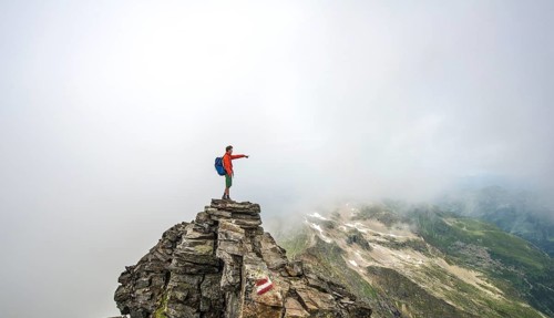 Hiker on the summit of the Hochgolling with rising fog