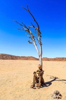 Cairn Lonely Man sits under a dried-up tree in Hartmann Valley