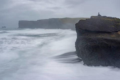 Couple stands above the Cliffs of Dyrholey at Storm