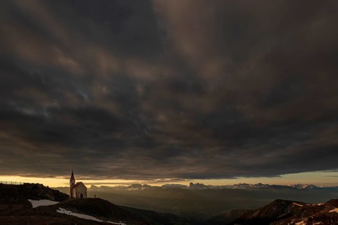 Latzfonser cross chapel at sunrise with dramatic clouds and South Tyrolean mountains