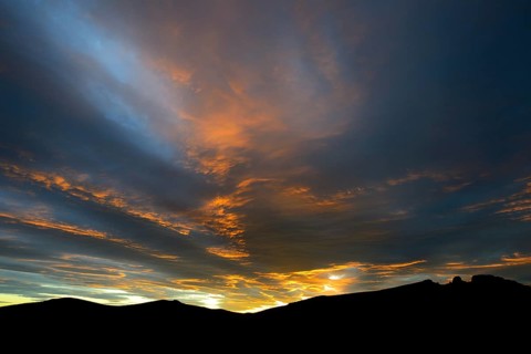 Dramatic sunset with rising storm clouds in front of mountain silhouette