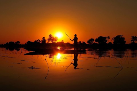 Local bargeman sails in traditional Mokoro dugout boat at sunset